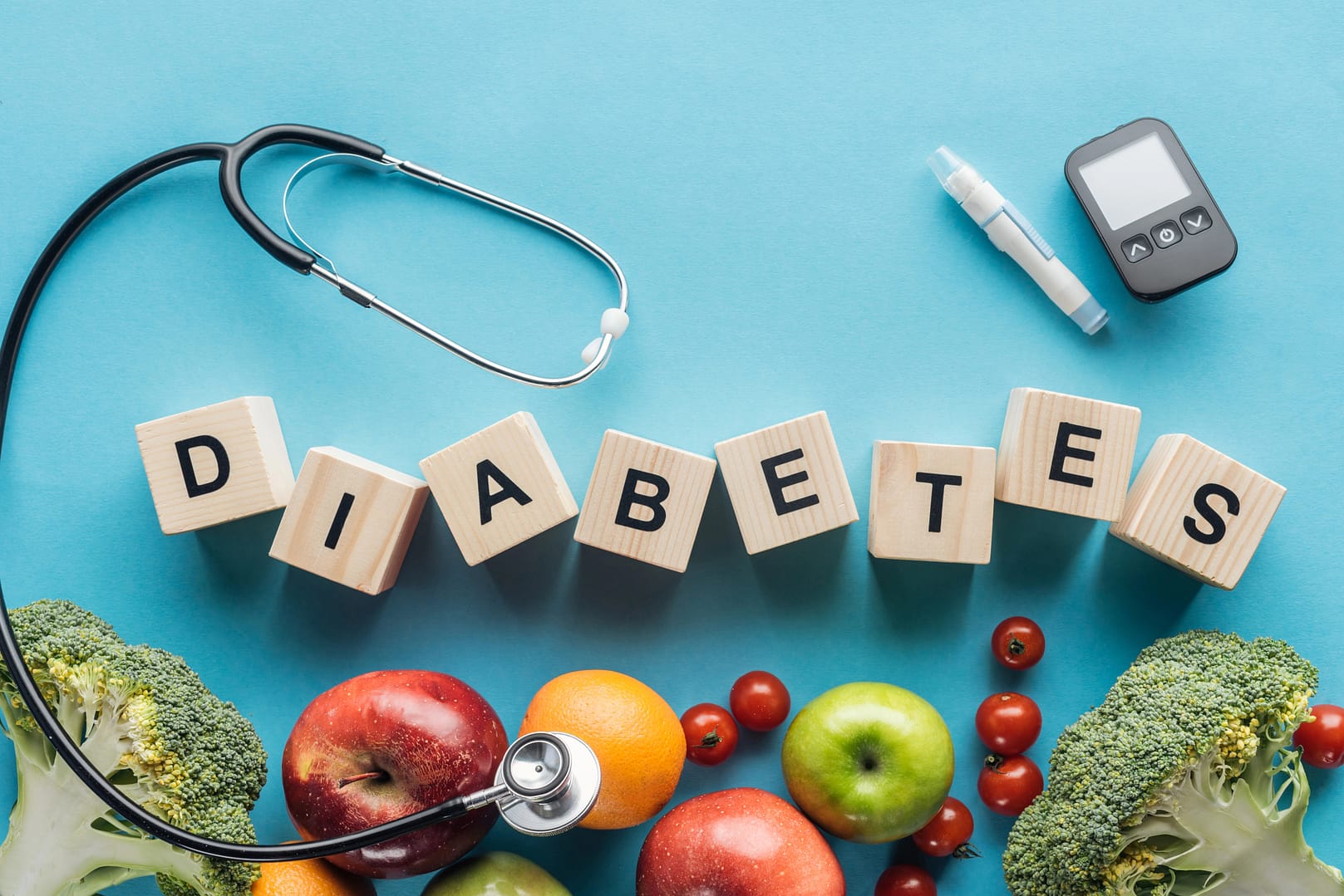 Holzklötze mit der Aufschrift „DIABETES“ sind mit einem Stethoskop, einem Blutzuckermessgerät und einer Reihe gesunder Früchte und Gemüse auf einem beruhigenden blauen Hintergrund gepaart.