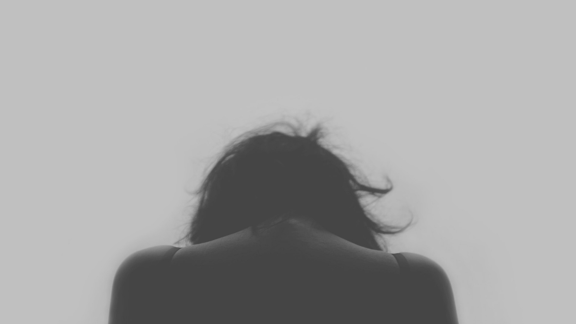 A black and white photo featuring a woman's back, conveying an aura of introspection or melancholy.